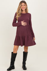 woman wearing a burgundy ribbed long sleeve maternity dress with a ruffled hem and holding her baby bump