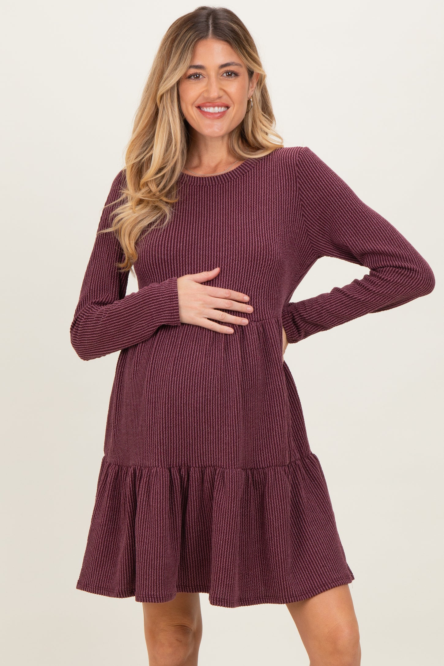 woman wearing a burgundy long sleeve maternity dress with a ruffled hem and posing with her baby bump