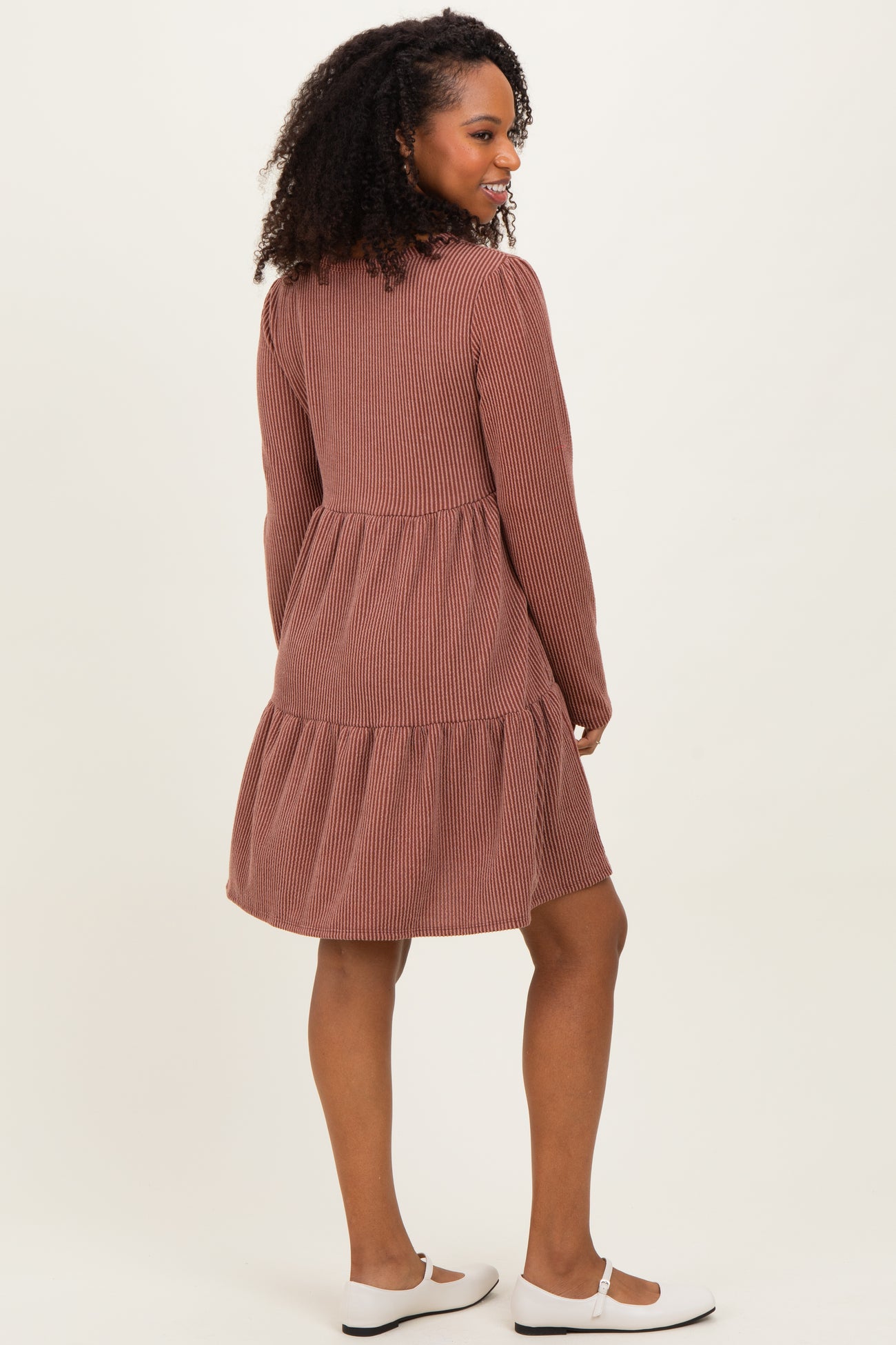 woman wearing a brown striped long sleeve dress with a tiered skirt and white flats, shown from the back