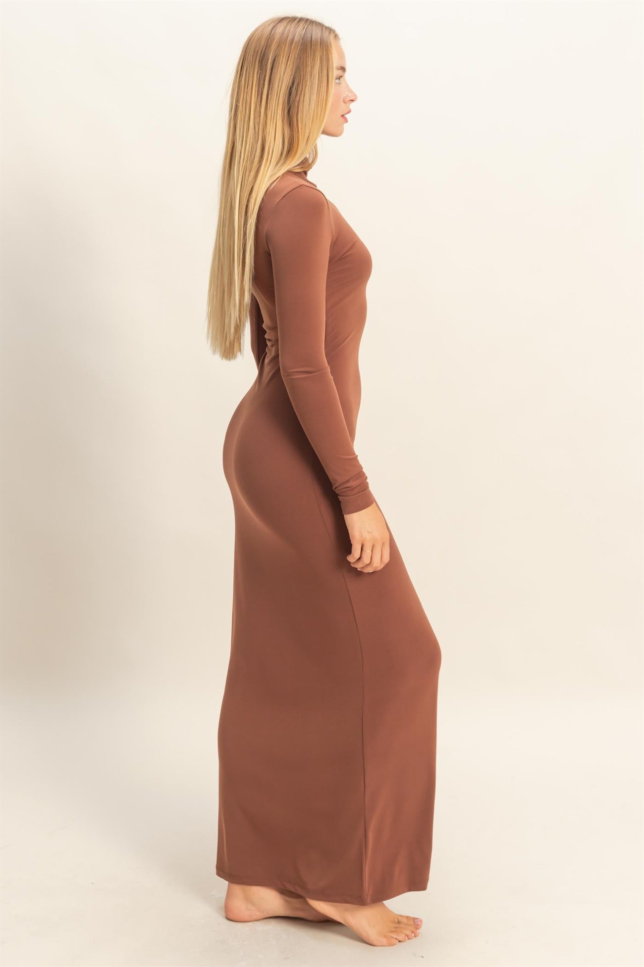 woman wearing a long brown fitted maxi dress, standing in profile with long hair down