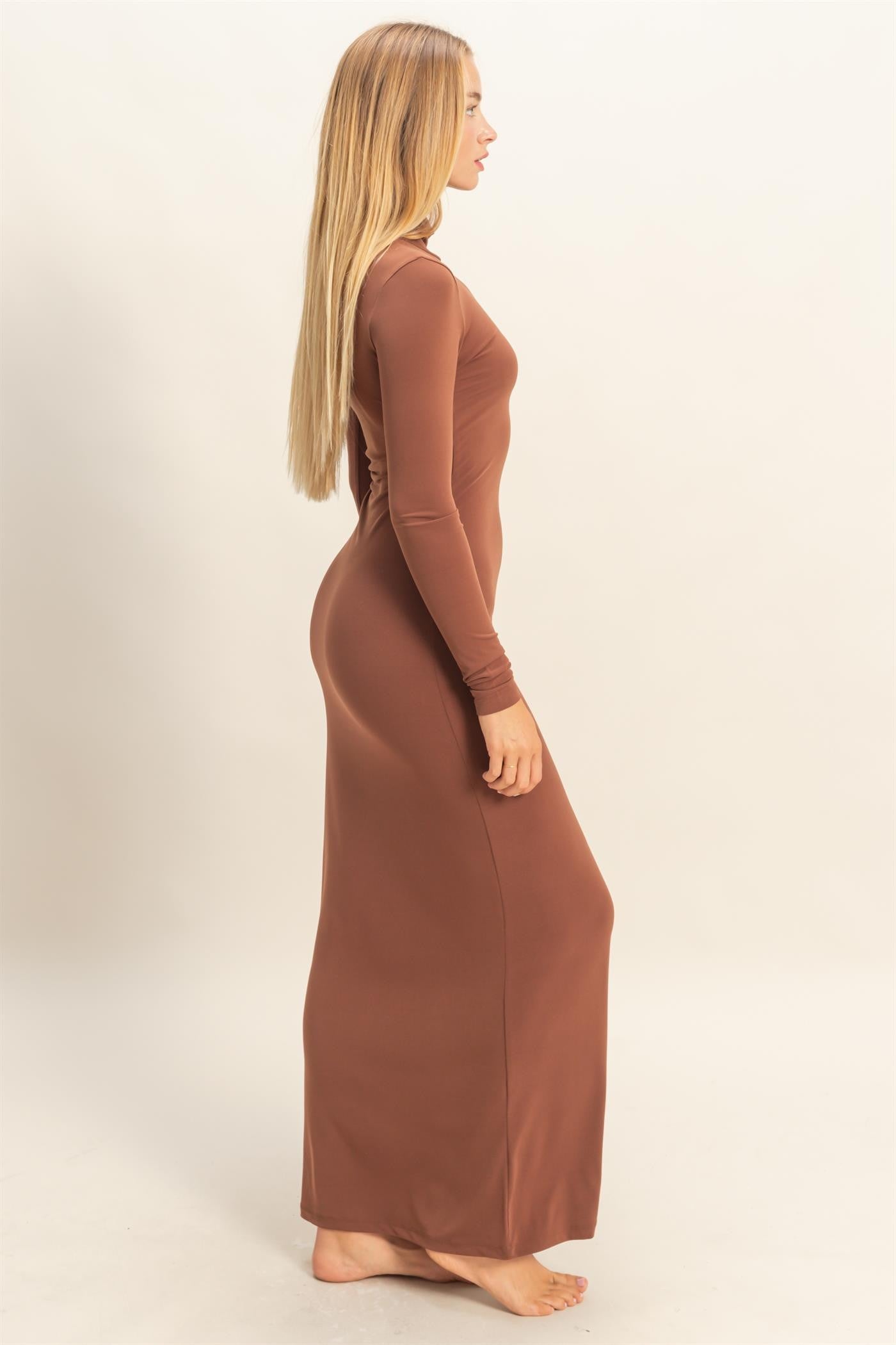 woman wearing a long brown fitted maxi dress, standing in profile with long hair down