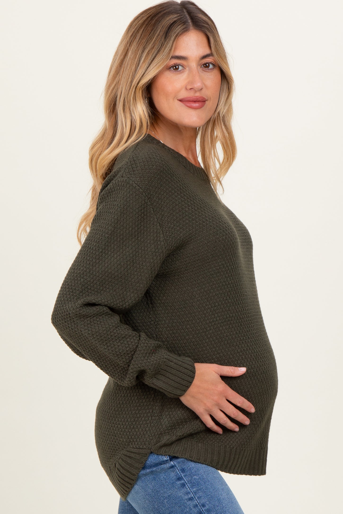 woman wearing a dark green textured maternity sweater and cradling her baby bump