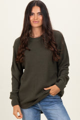 woman wearing a dark green textured sweater with long sleeves and relaxed fit, paired with light blue jeans