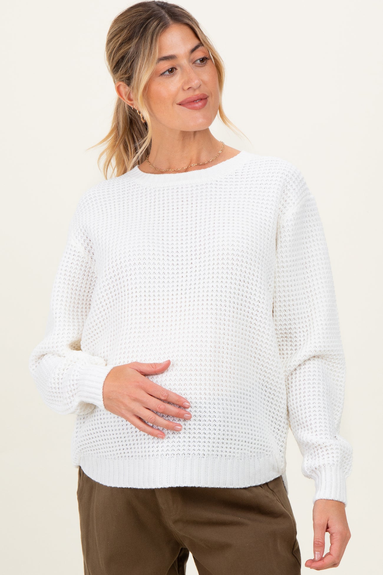 woman wearing a white knit maternity sweater and holding her baby bump