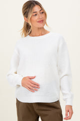 woman wearing a white knit maternity sweater and holding her baby bump