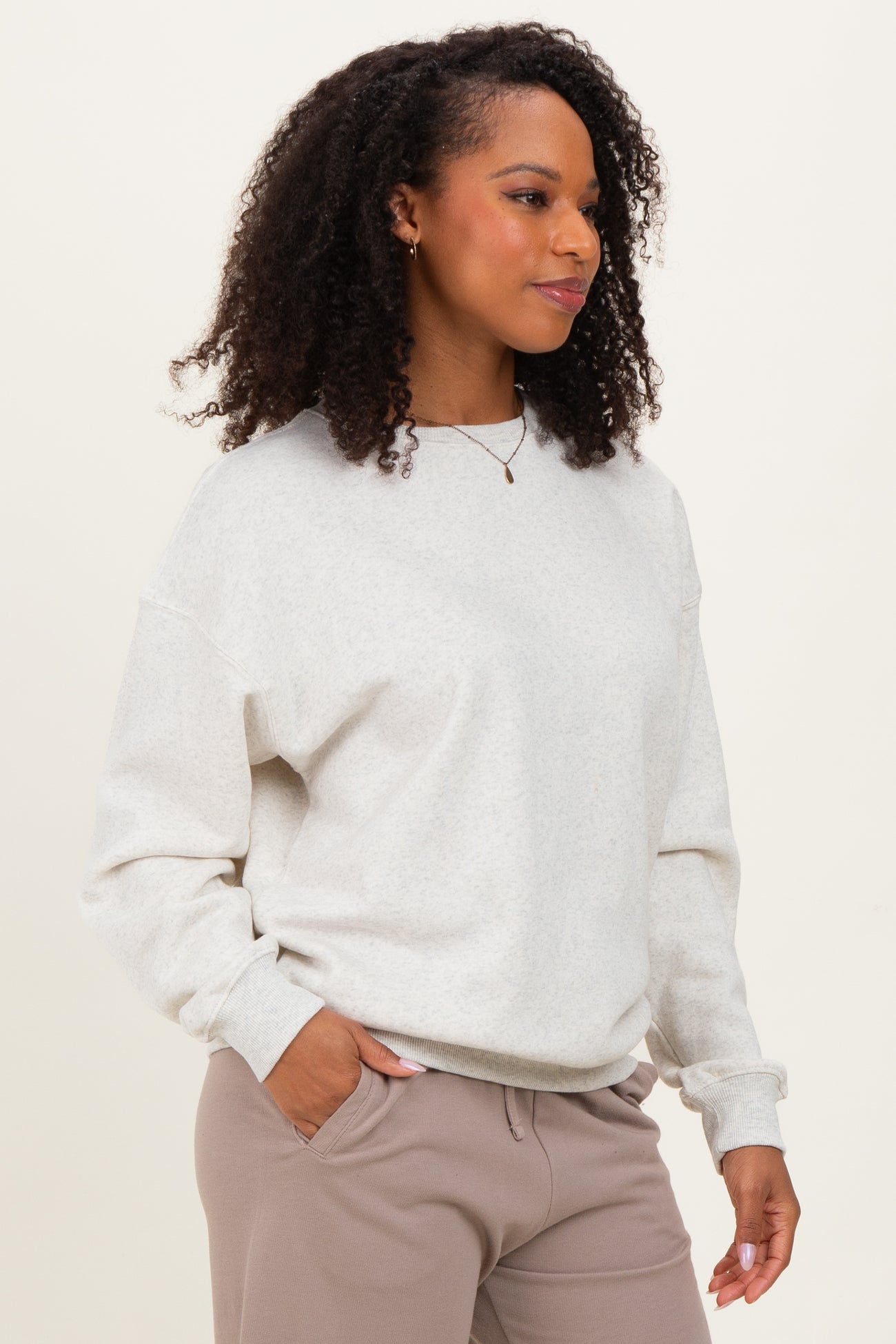 woman wearing a light gray oversized sweatshirt with long sleeves and relaxed fit, styled with neutral pants