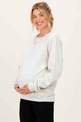 woman wearing a light gray maternity sweatshirt and holding her baby bump
