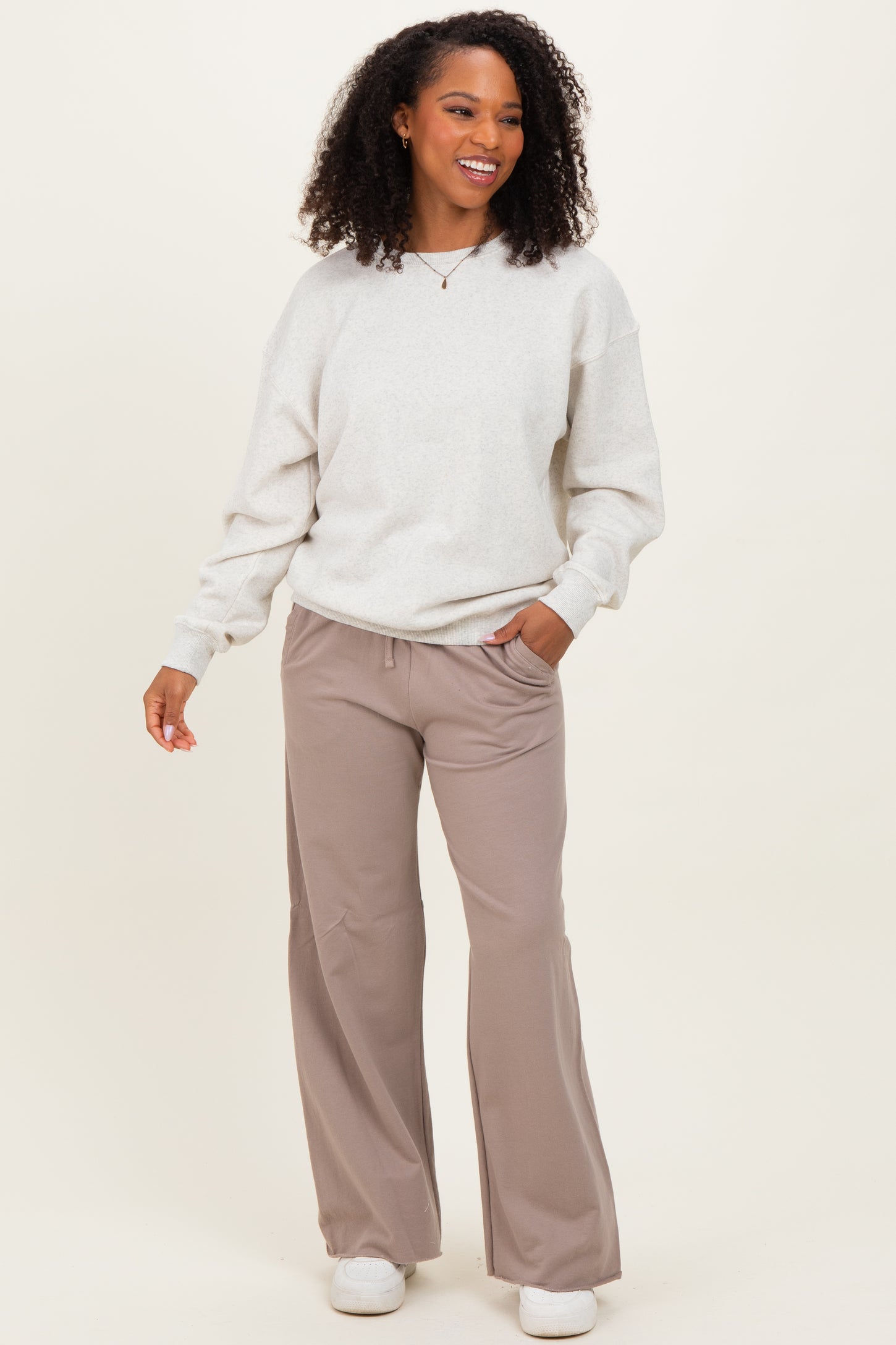 woman wearing a light gray oversized sweatshirt and beige wide-leg pants, standing with hands in pockets