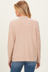 woman wearing a light pink maternity sweater with a relaxed fit and slightly open back, styled with blue jeans