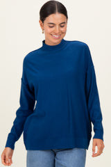 woman wearing a blue high neck sweater with a relaxed fit and long sleeves, smiling against a neutral background