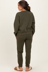 woman wearing a dark olive green maternity sweatsuit standing with back to the camera