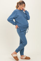 woman wearing a blue maternity sweatshirt and matching joggers, with a visible baby bump and slippers