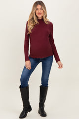 woman wearing a burgundy ribbed maternity top and blue skinny jeans, showing her baby bump, with black knee-high boots