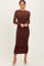 woman wearing a chocolate brown long sleeve ruched midi dress with a sheer bodice and fitted silhouette