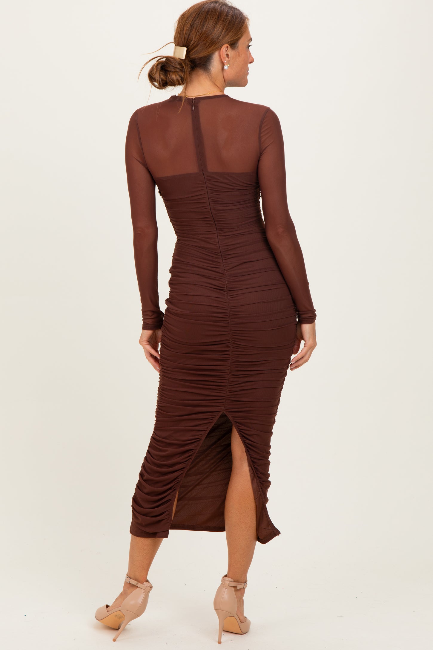 woman wearing a brown long sleeve ruched midi dress with a side slit and sheer panels on the sleeves