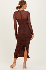woman wearing a brown long sleeve ruched midi dress with a side slit and sheer panels on the sleeves