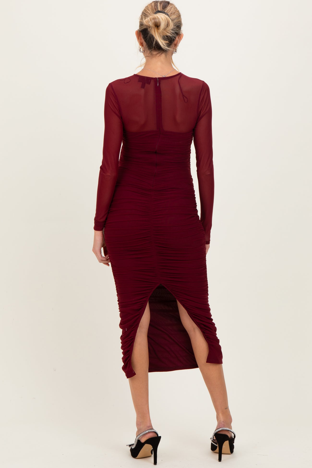 woman wearing a burgundy maternity dress with long sleeves, ruching details, and side slits, showing a baby bump