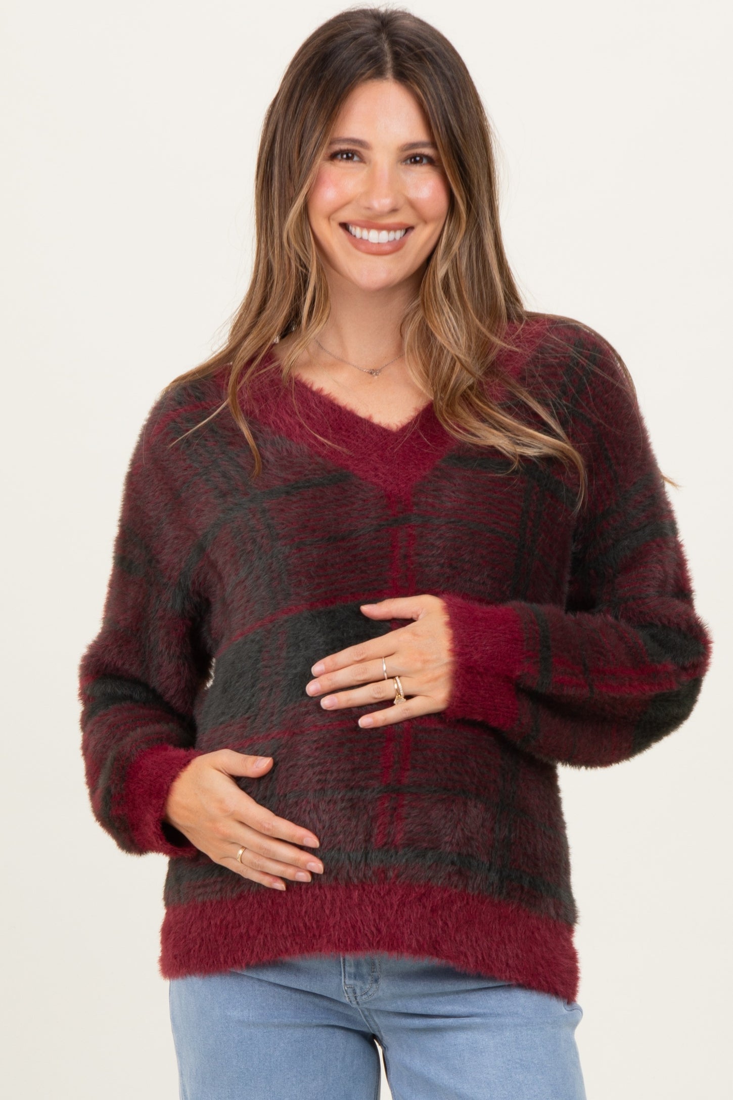 woman wearing a burgundy and black plaid maternity sweater and holding her baby bump