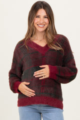 woman wearing a burgundy and black plaid maternity sweater and holding her baby bump