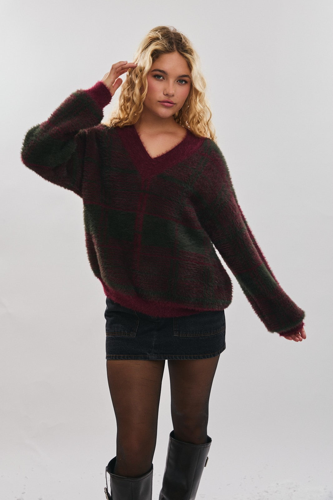 woman wearing a burgundy and green plaid oversized sweater with a v-neck and a denim skirt