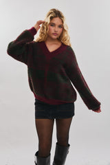 woman wearing a burgundy and green plaid oversized sweater with a v-neck and a denim skirt