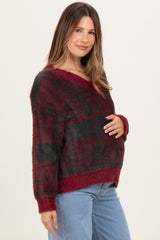 woman wearing a burgundy and black plaid maternity sweater and holding her baby bump