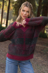 woman wearing a cozy burgundy and gray checkered maternity sweater with a v-neck, smiling outdoors in a forest setting