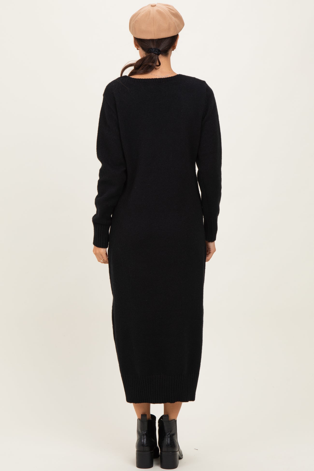 woman wearing a black long sleeve sweater dress, viewed from the back, paired with a beige beret and black ankle boots