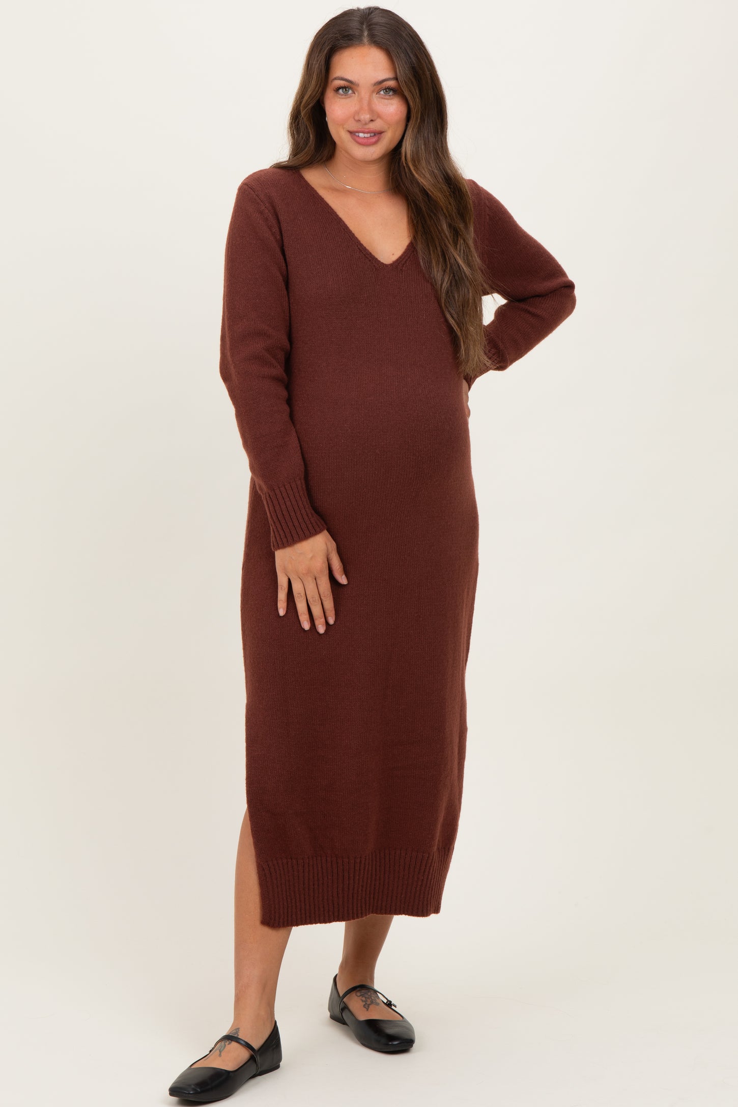 woman wearing a rust-colored long sleeve maternity dress with a v-neck and side slit, showing her baby bump