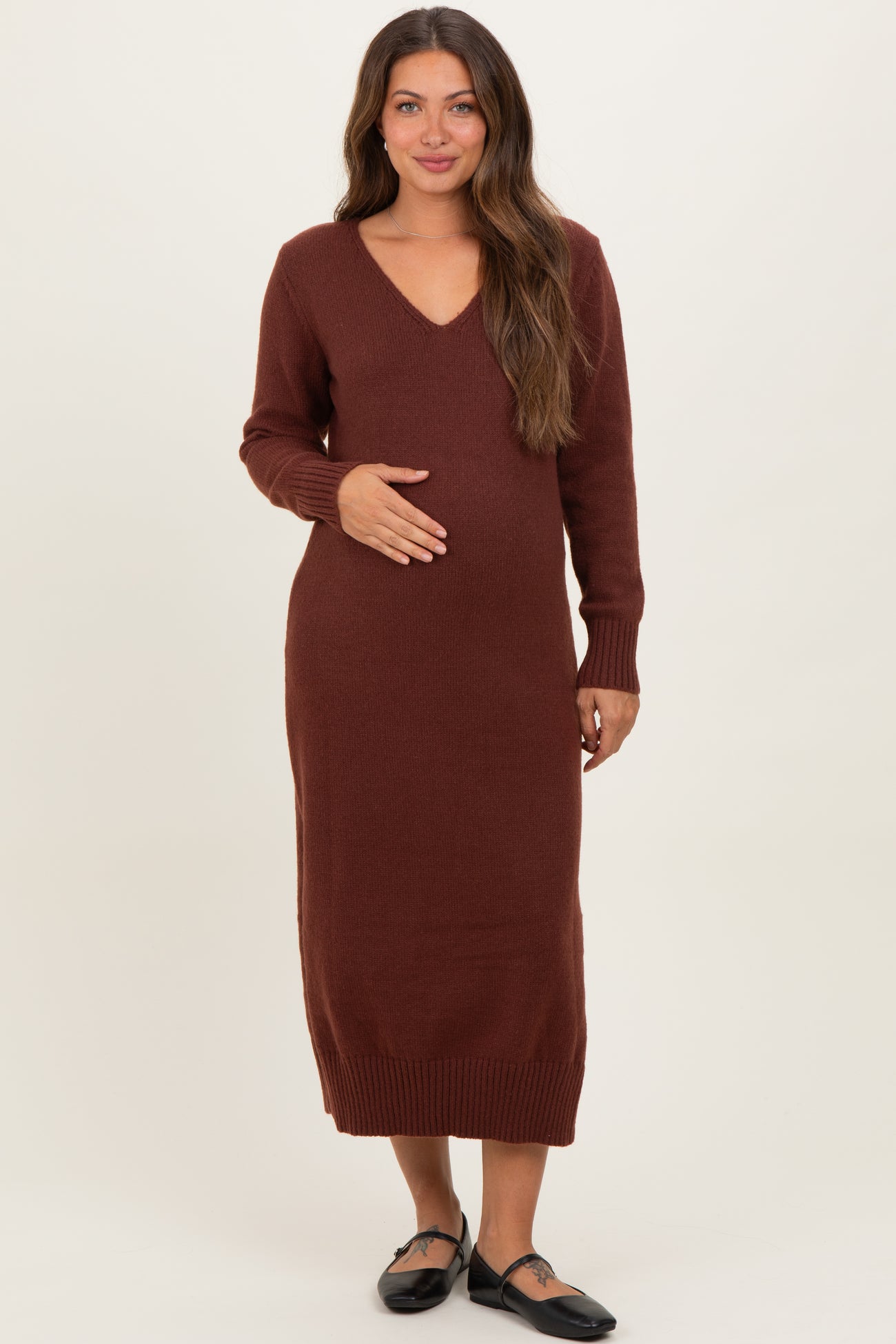 woman wearing a burgundy long sleeve maternity dress with a v-neck and holding her baby bump