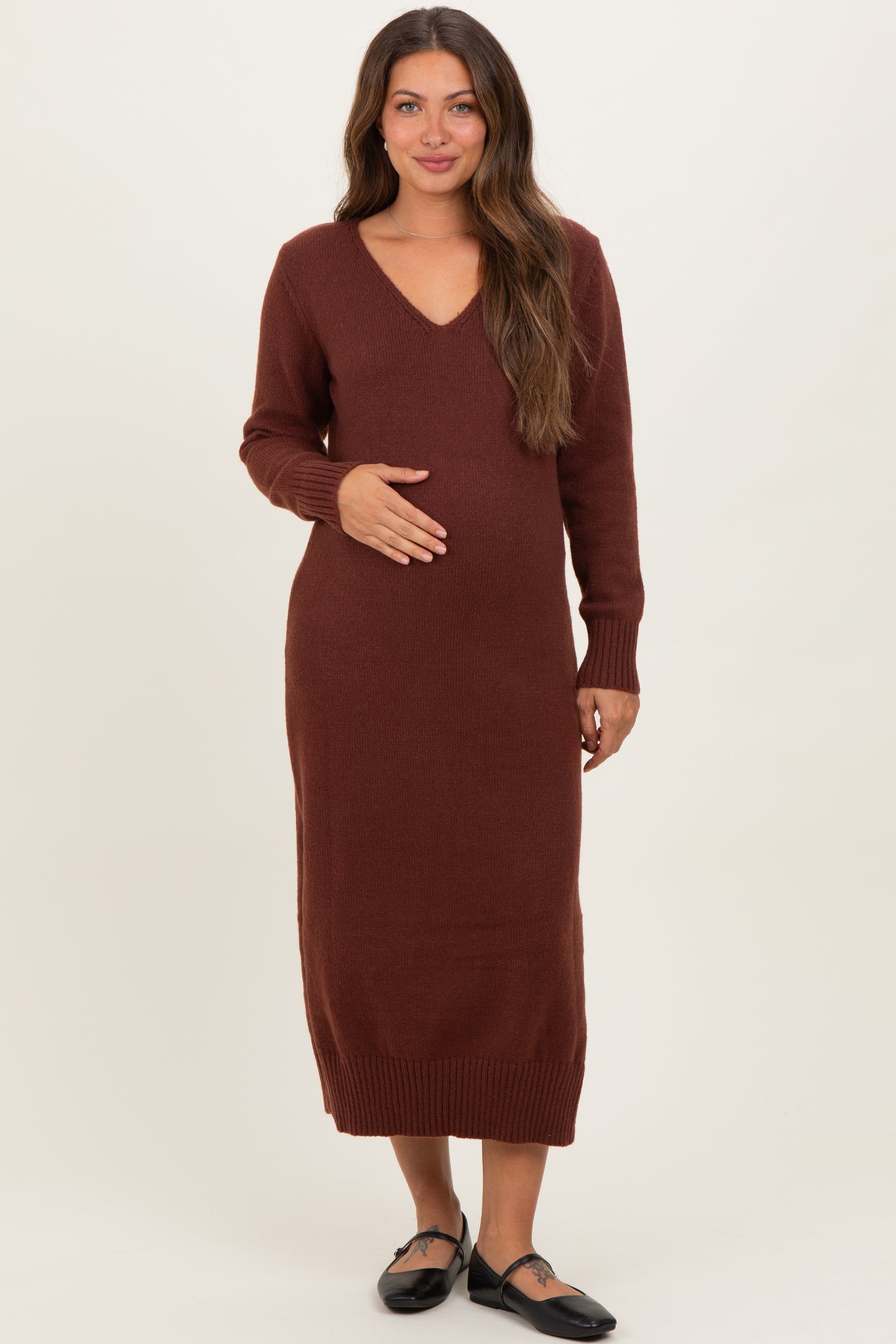 woman wearing a burgundy long sleeve maternity dress with a v-neck and holding her baby bump