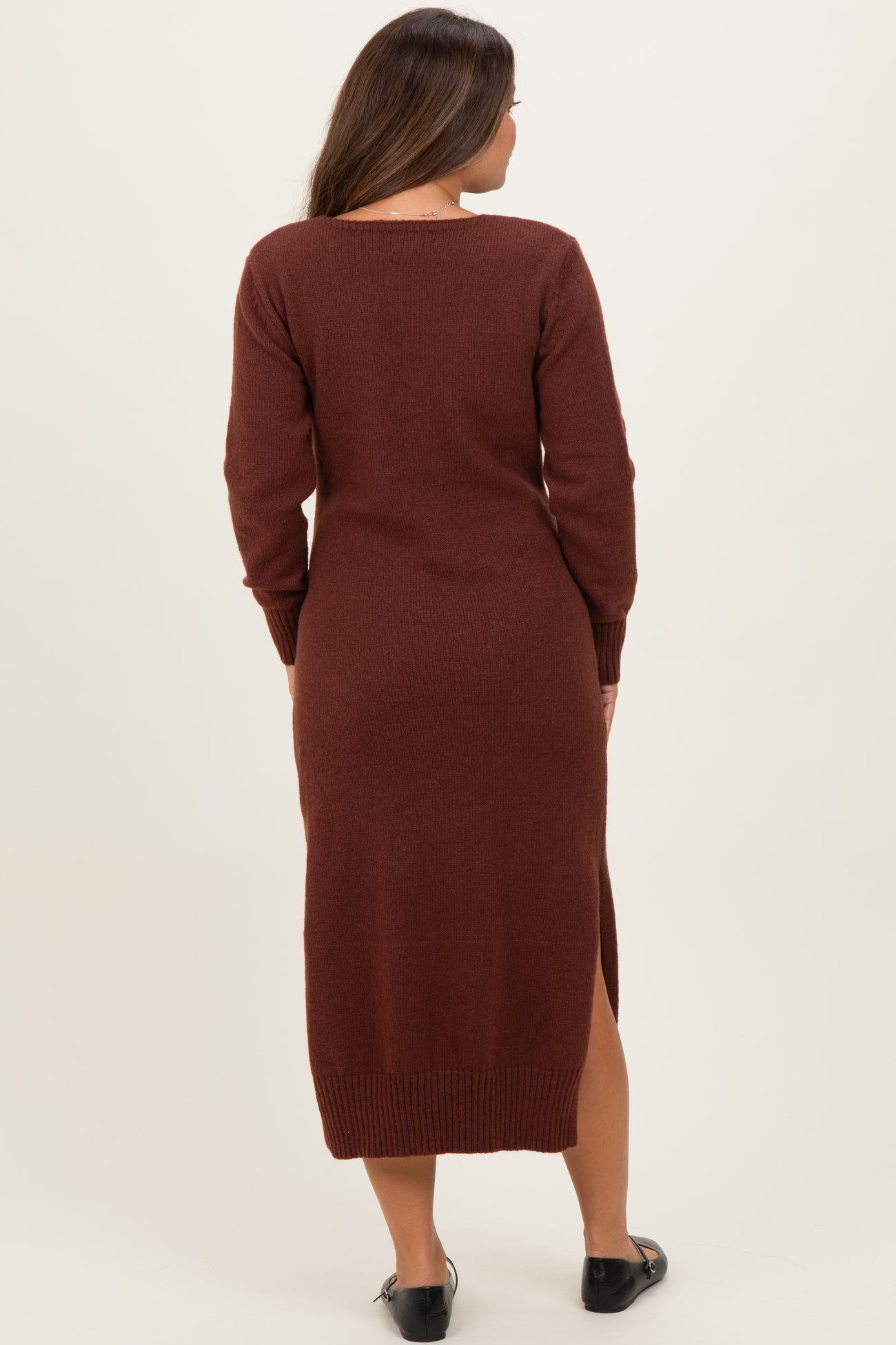 woman wearing a rust long sleeve maternity sweater dress with side slits and a fitted silhouette