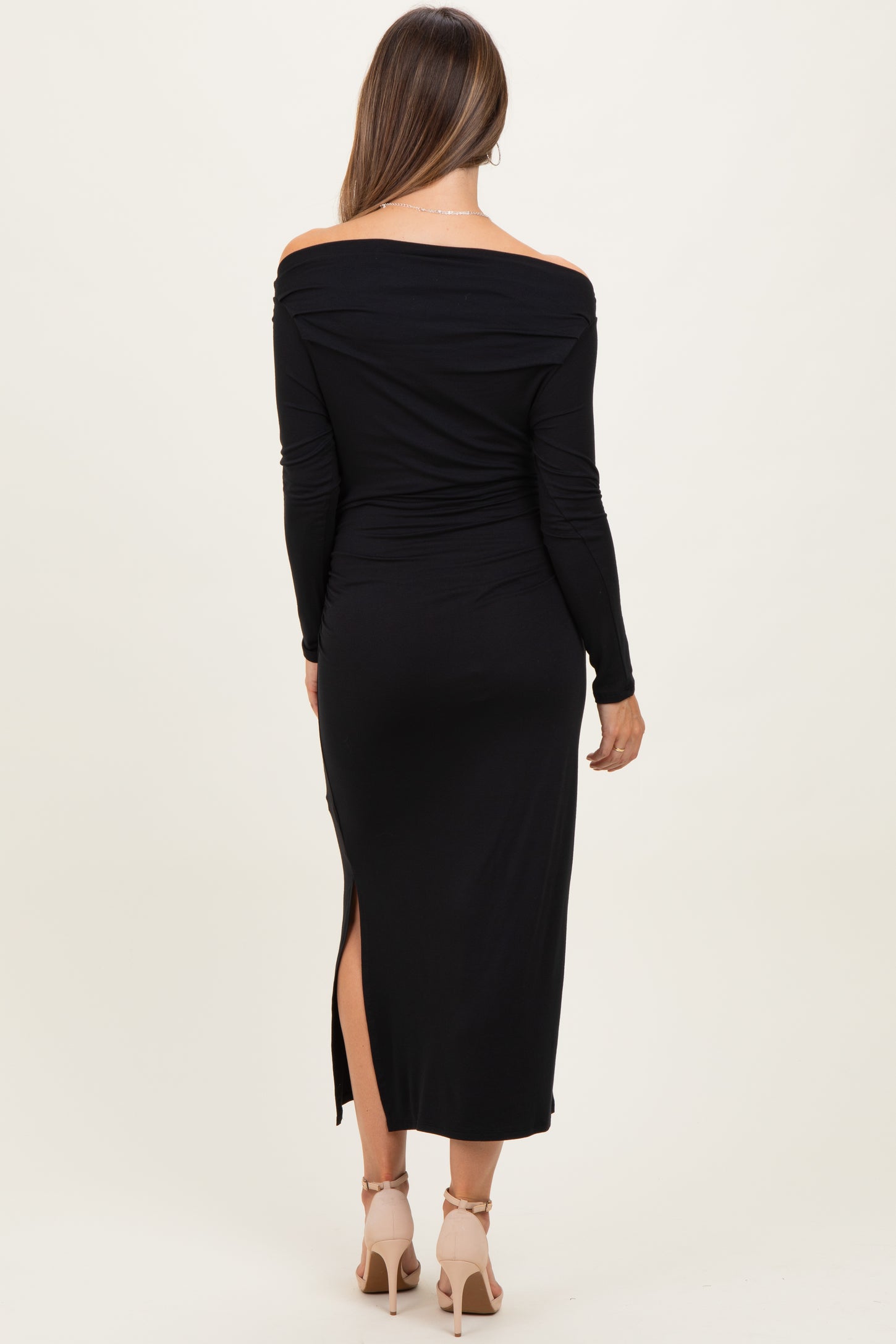 woman wearing a black off-shoulder maternity dress with a side slit, showing her baby bump from the back