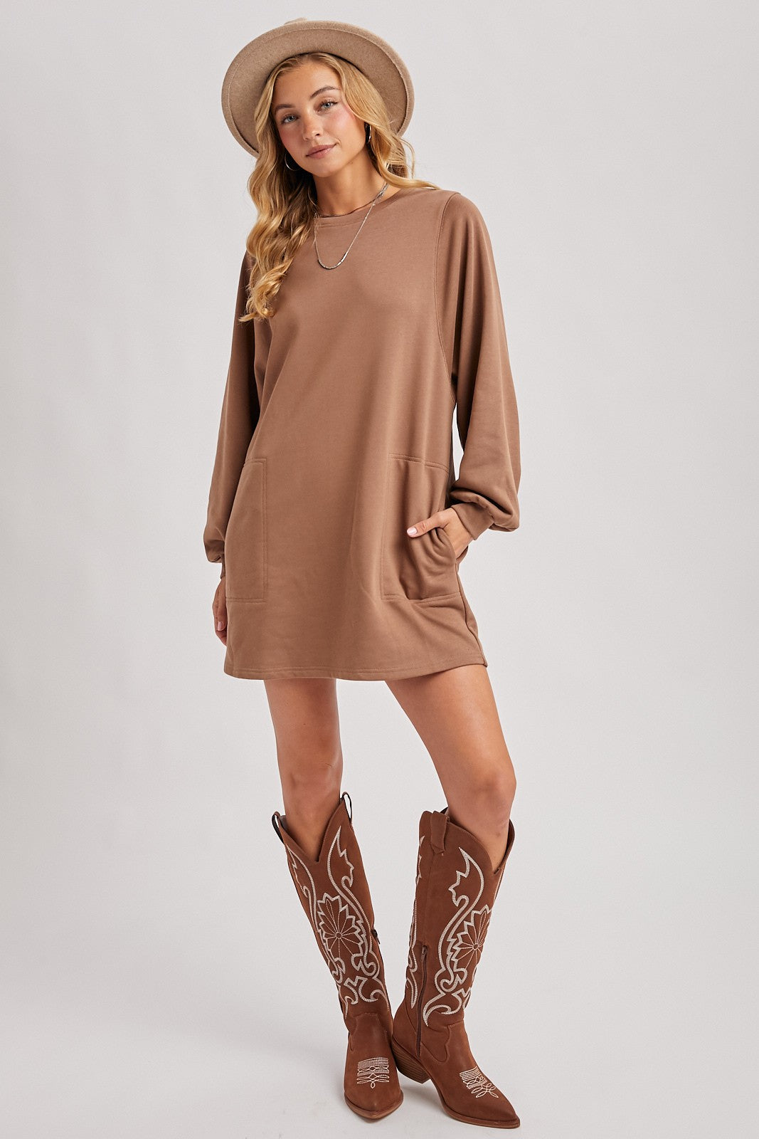 woman wearing a brown long sleeve sweatshirt dress with pockets and brown embroidered cowboy boots