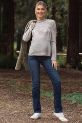 woman wearing a striped long sleeve maternity top with a round neckline and blue maternity jeans, standing outdoors