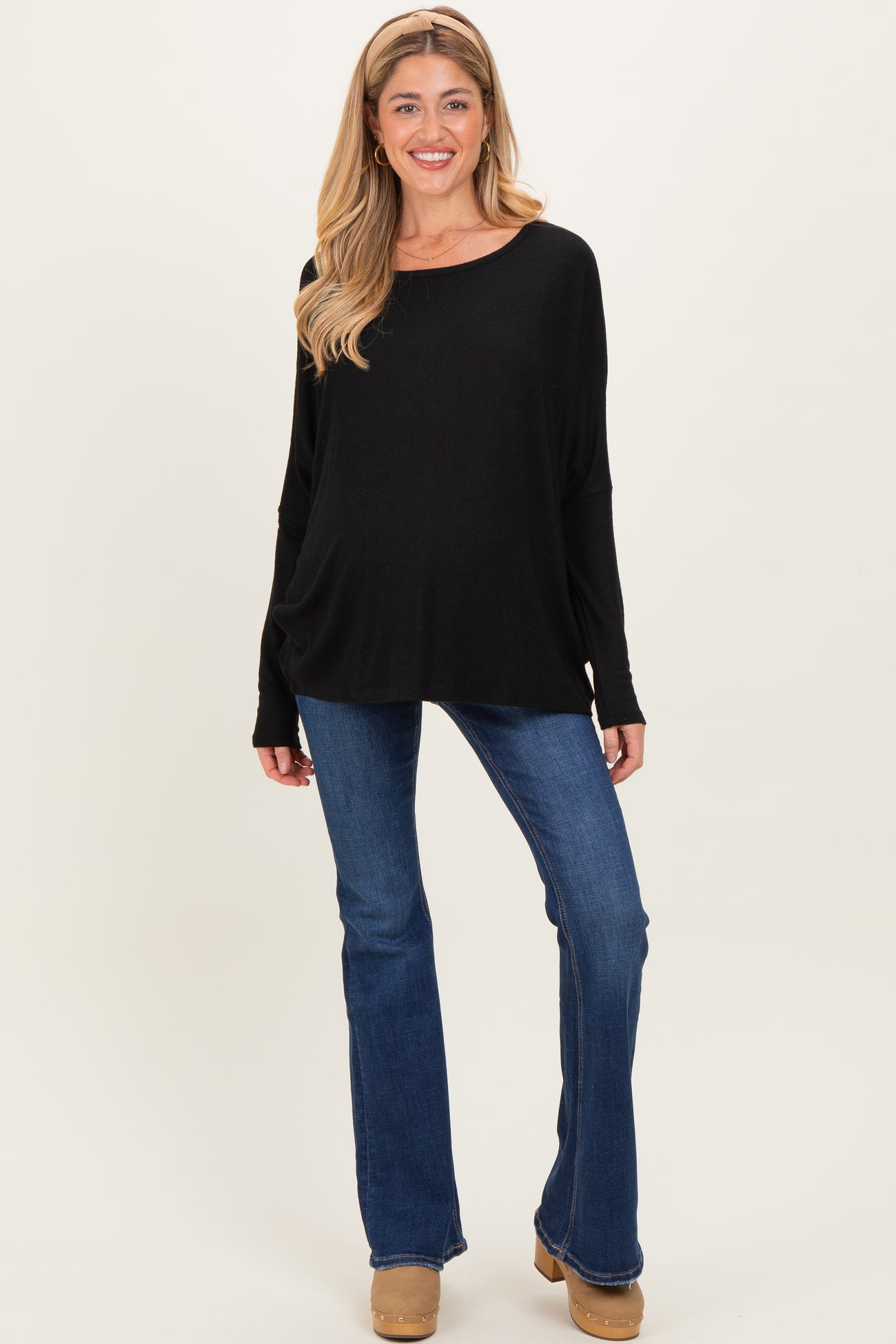 woman wearing a black maternity top with long sleeves and a relaxed fit, paired with blue flared maternity jeans and smiling