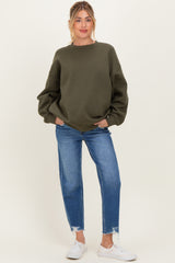 woman wearing an olive green oversized sweatshirt and blue distressed jeans, styled as maternity wear