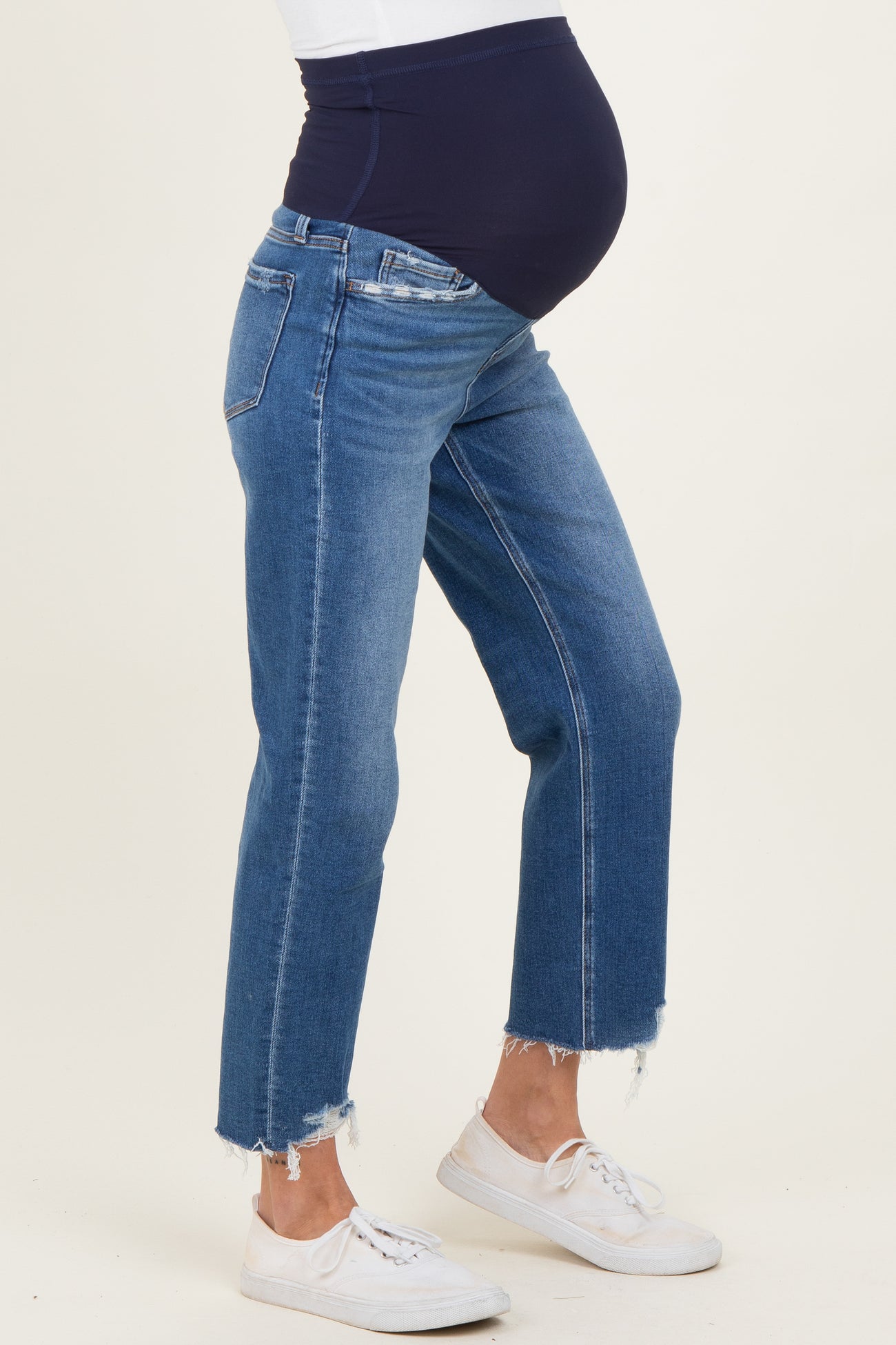 woman wearing a pair of distressed blue maternity jeans with a navy belly panel and a visible baby bump