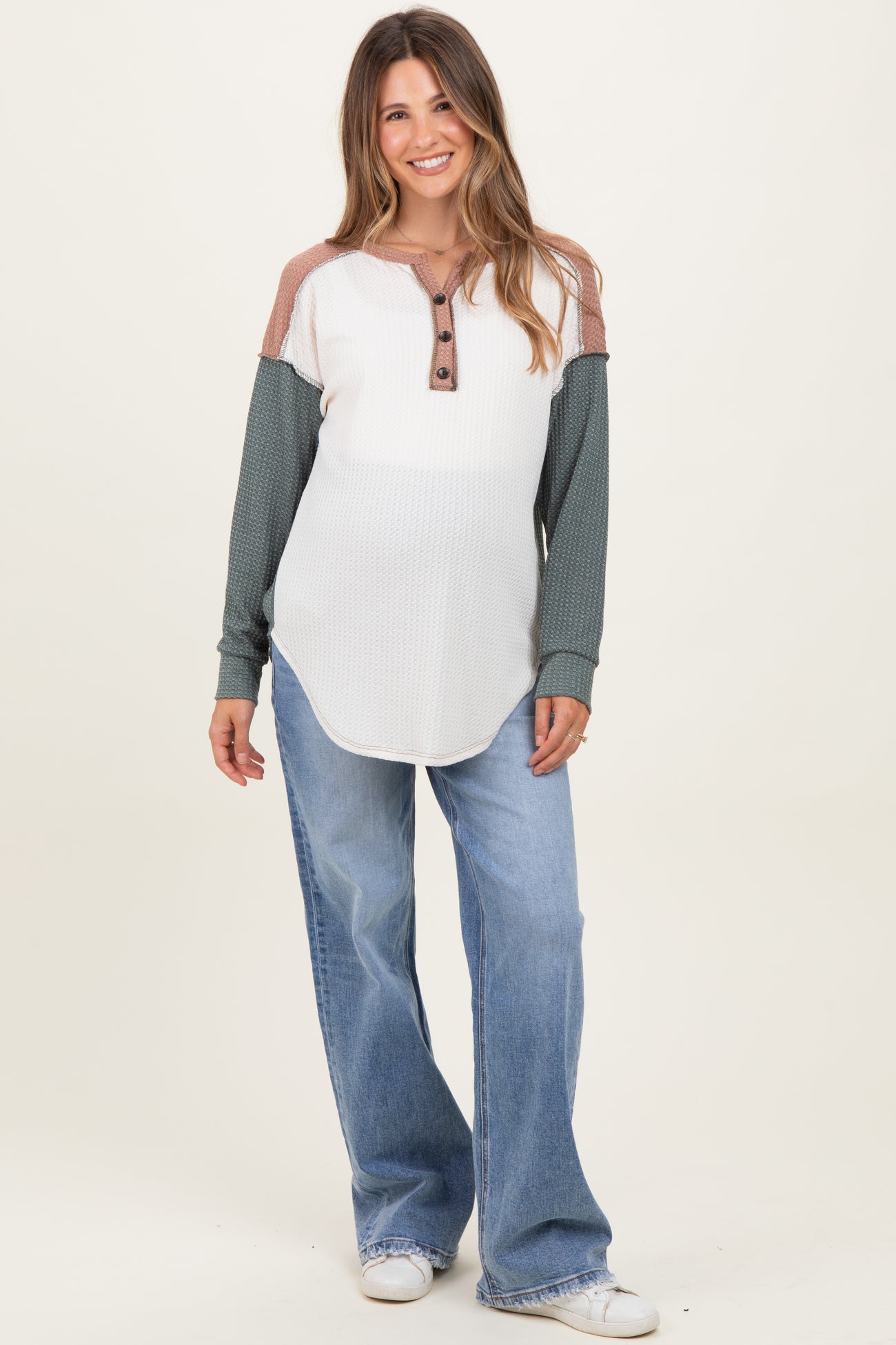 woman wearing a white and green long sleeve maternity top with buttons and paired with loose blue jeans
