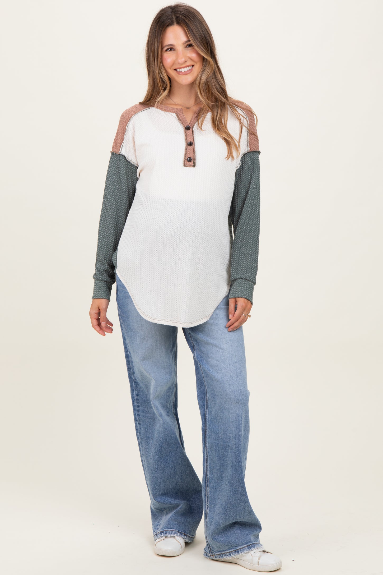woman wearing a white and green long sleeve maternity top with buttons and paired with loose blue jeans