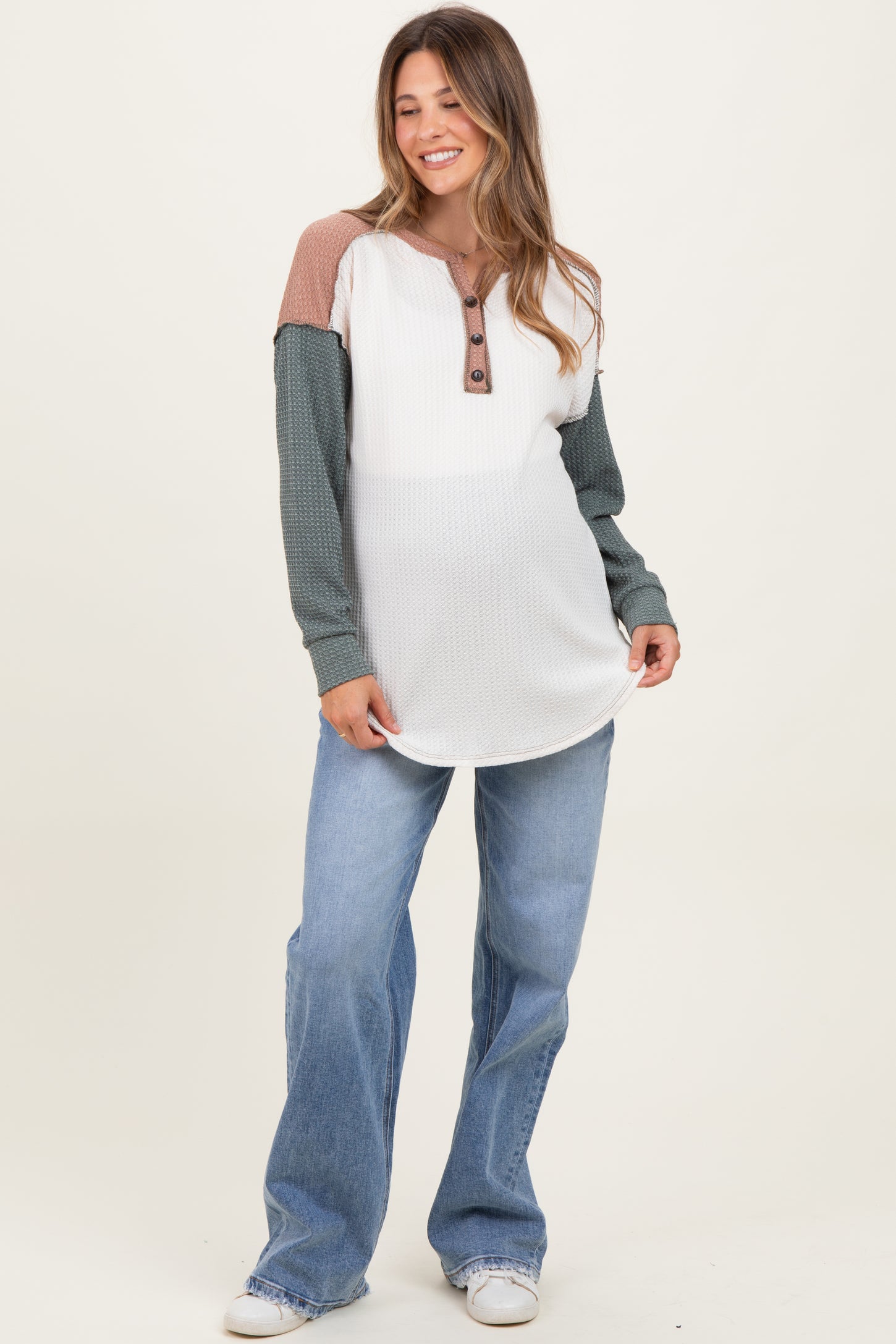 woman wearing a color-blocked maternity top in white, rust, and green, paired with wide-leg jeans and smiling
