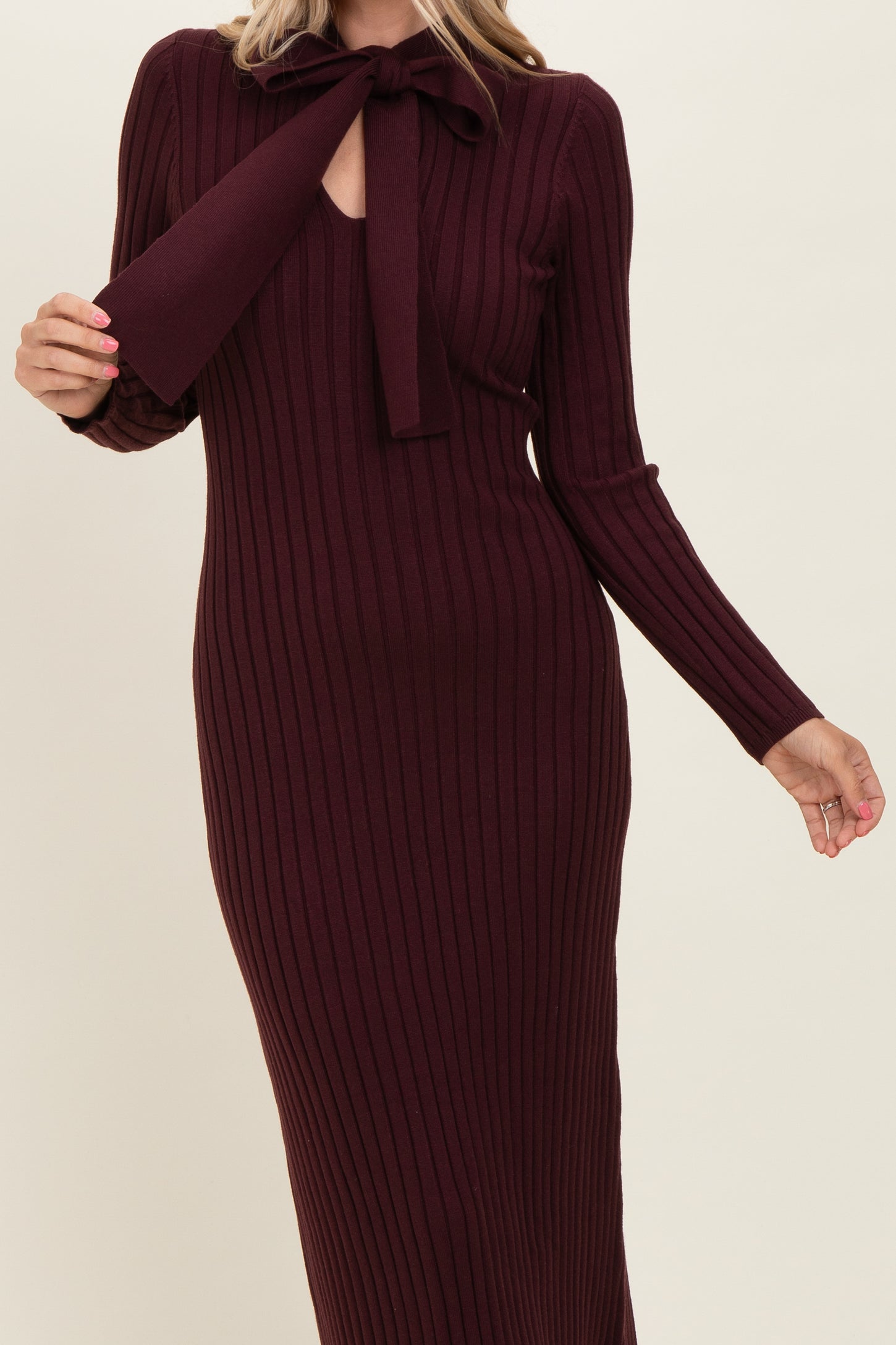 woman wearing a burgundy ribbed knit maxi dress with a bow tie neckline and long sleeves