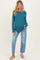 woman wearing a teal ribbed maternity sweater with a baby bump and light blue distressed jeans