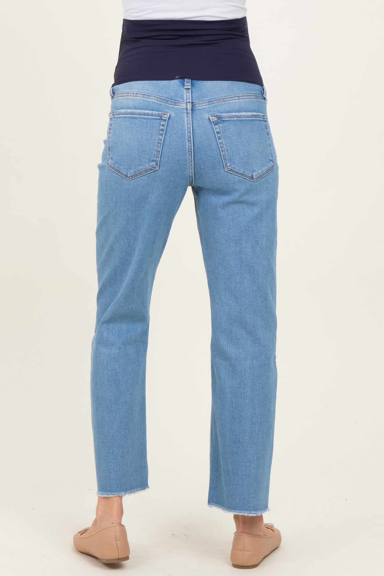 woman wearing light wash maternity jeans with a stretchy navy waistband and cropped hem, showing the back view