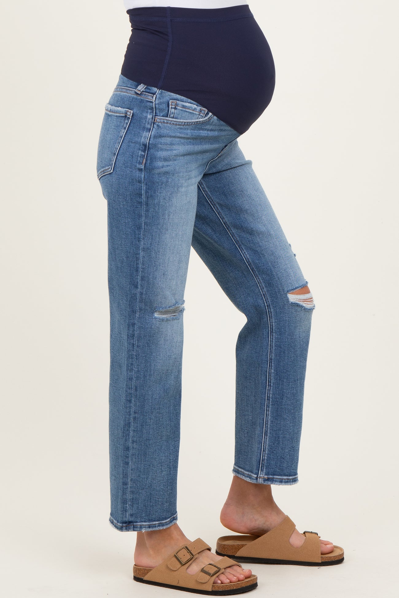 maternity wear in light blue distressed jeans with a navy belly panel, model showing baby bump and wearing tan sandals