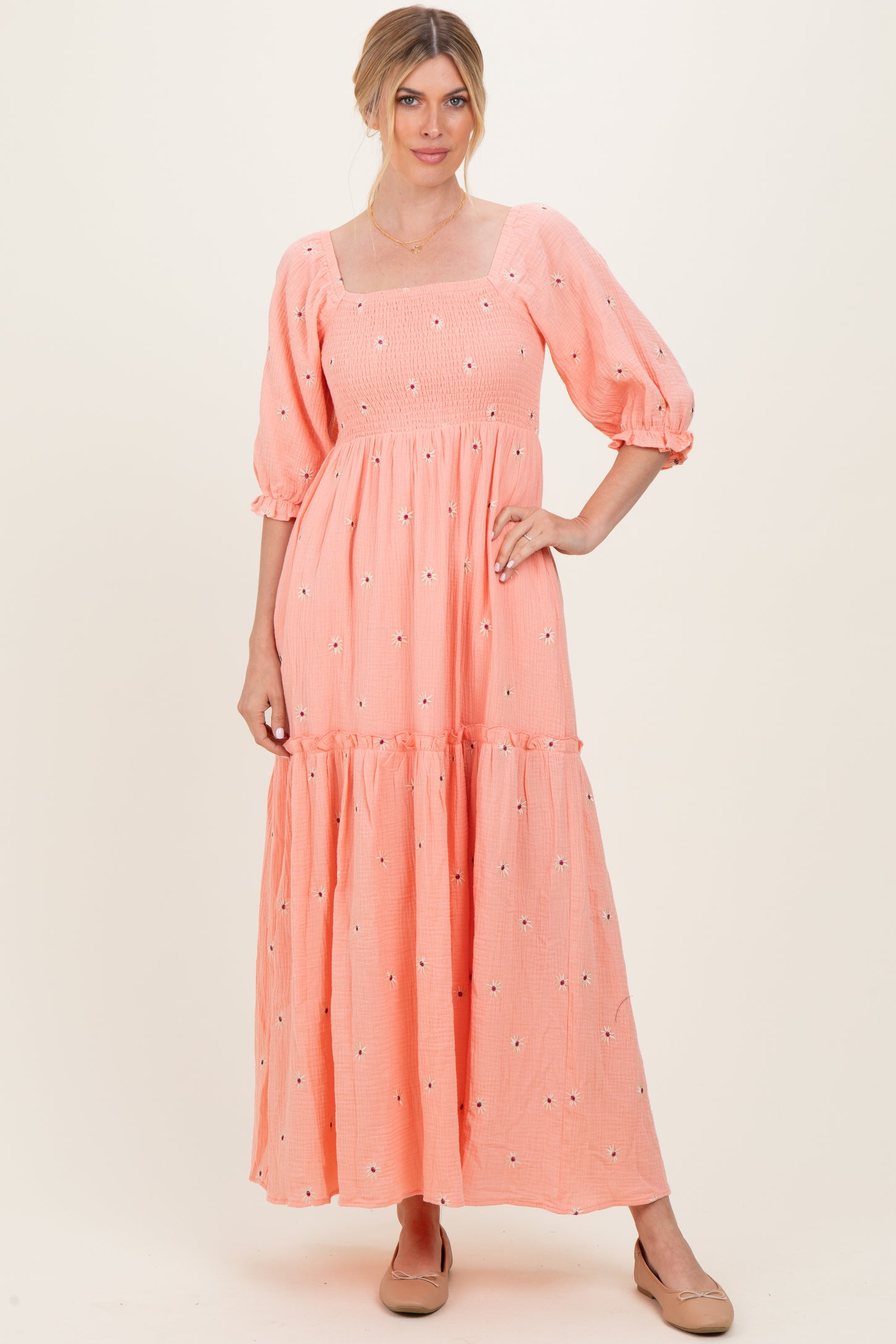 woman wearing a coral tiered maxi dress with puff sleeves and floral embroidery