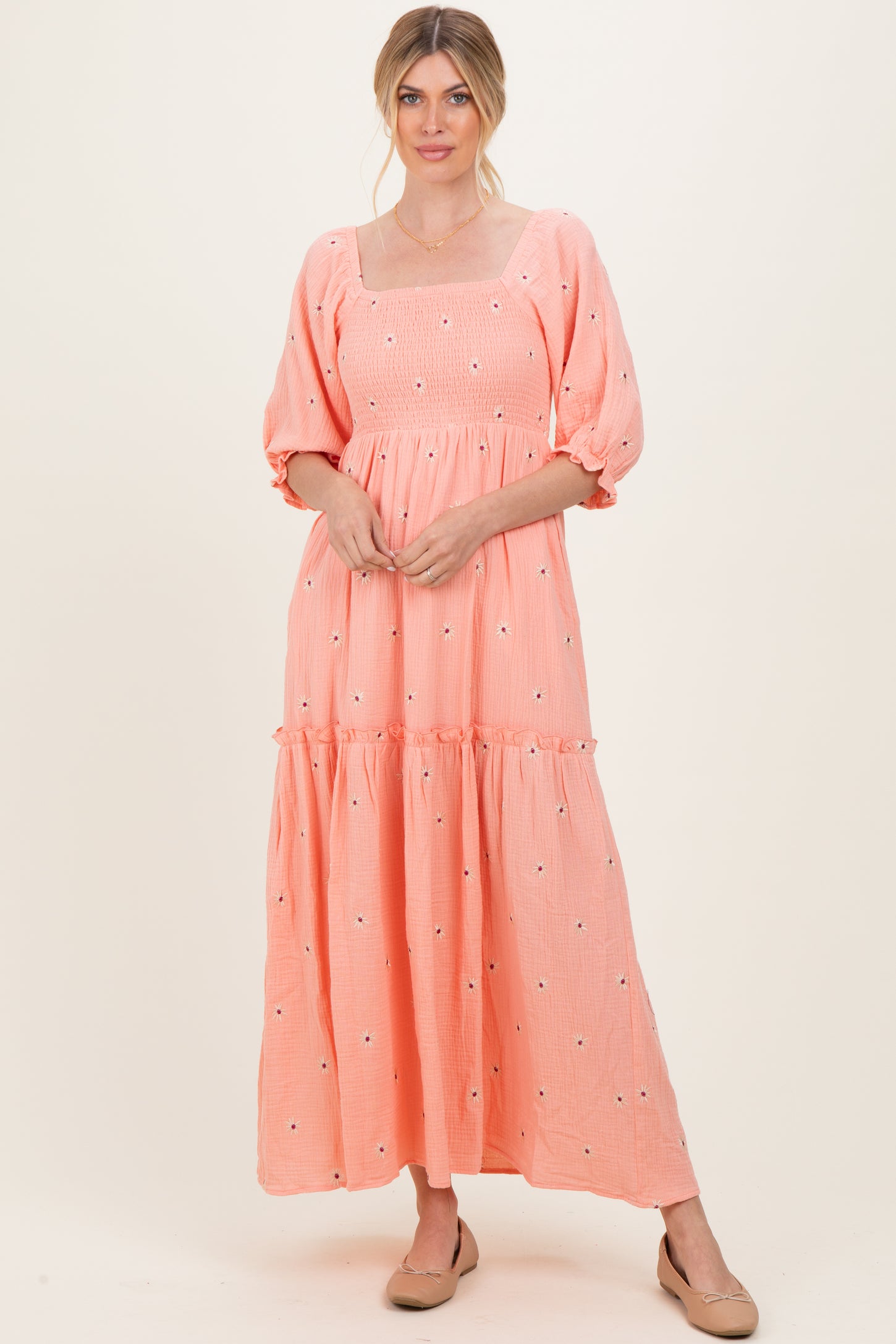 woman wearing a peach puff sleeve maxi dress with floral embroidery and a tiered skirt