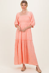 woman wearing a peach puff sleeve maxi dress with floral embroidery and a tiered skirt
