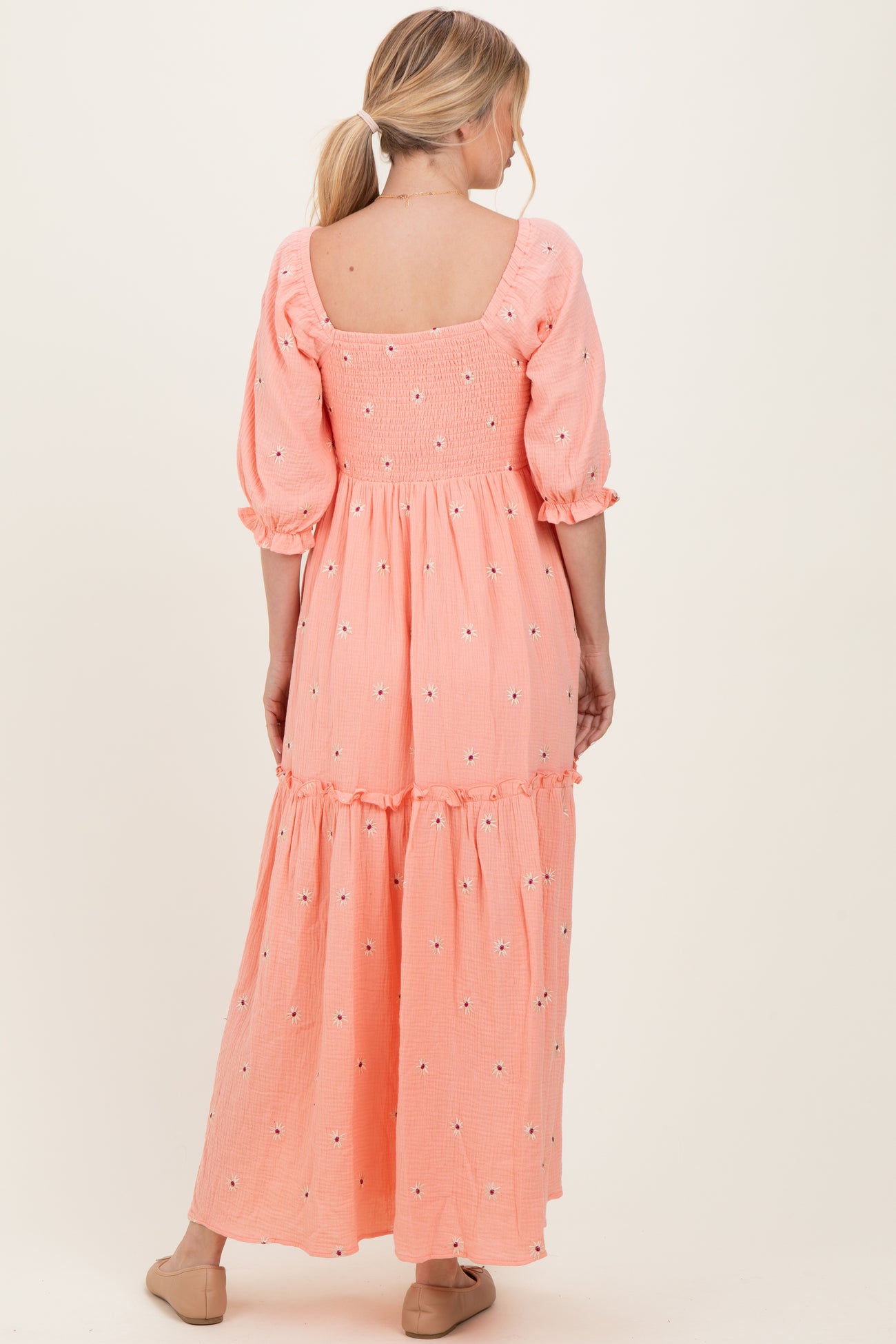 woman wearing a pink maxi dress with puff sleeves and embroidered floral details, showing the back view
