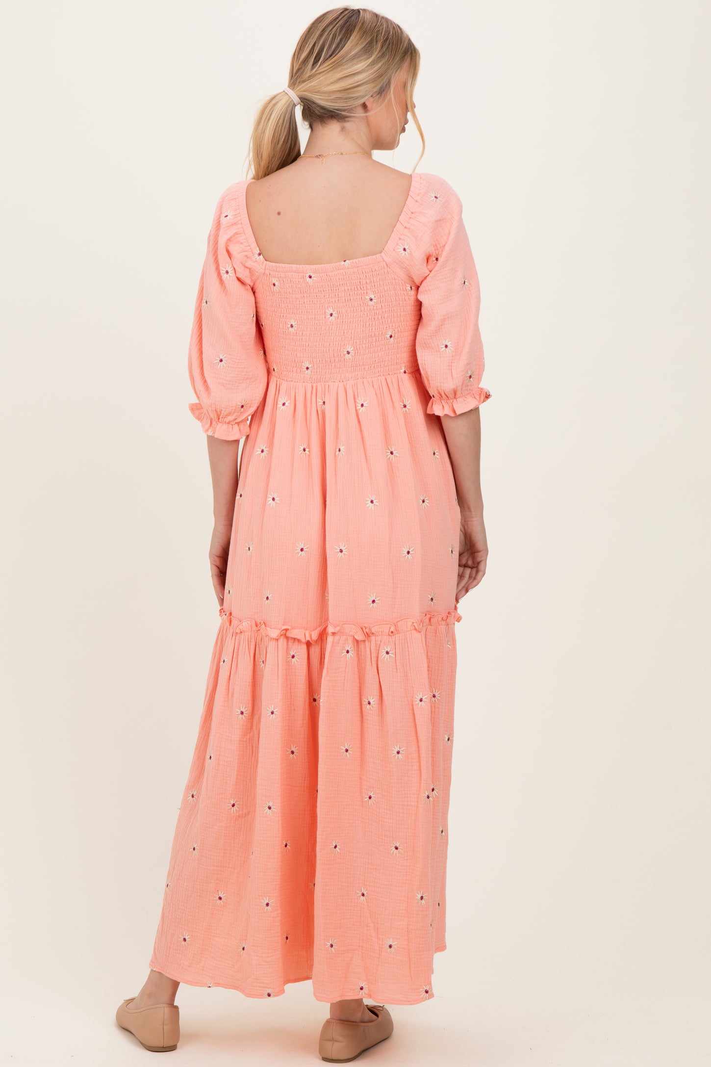 woman wearing a pink maxi dress with puff sleeves and embroidered floral details, showing the back view
